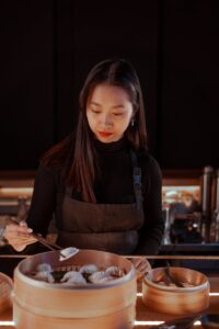 Une femme asiatique dans la cuisine d'un restaurant prépare soigneusement des boulettes, mettant en valeur ses compétences culinaires.