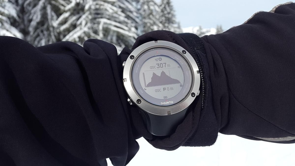 Montre connectée montrant une montagne sur son écran, portée sur un bras ganté Montre connectée montrant une montagne sur son écran, portée sur un bras ganté
